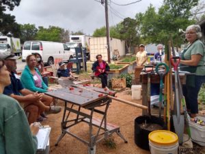 people listening to a tool care workshop with lots of garden tools being displayed
